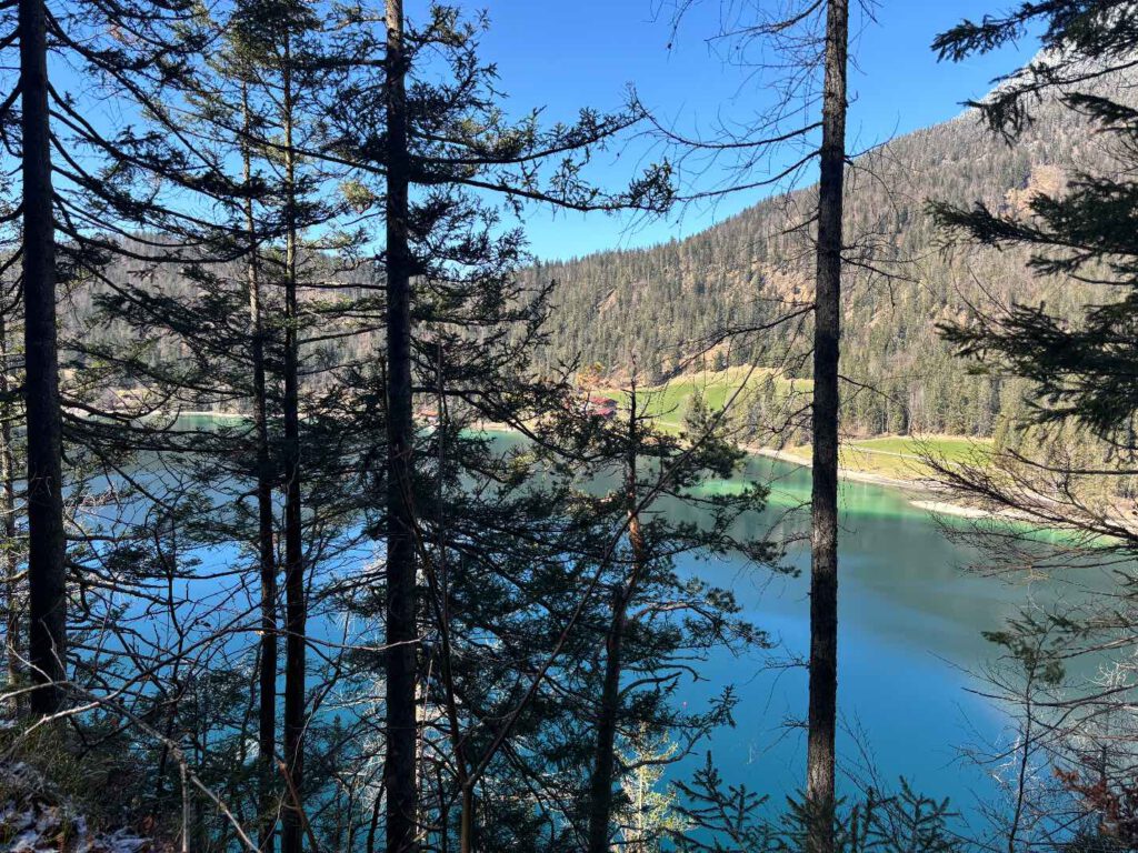 Hintersteiner See im Frühling, Aussicht auf einen klaren See, umgeben von Nadelbäumen und Berglandschaft, unter strahlend blauem Himmel.