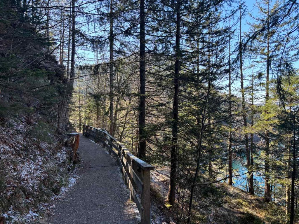 Hintersteiner See im Frühling, Ein schmaler Pfad umgeben von Bäumen, mit einem Holzgeländer, das entlang eines Hanges führt.